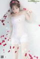 A woman in a white bathing suit laying in a bathtub with rose petals.