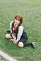 A woman in a school uniform sitting on a soccer field.