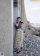 A woman leaning against a wall on a rocky beach.