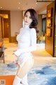 A woman in a white dress and thigh high boots posing for the camera.