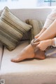 A woman sitting on a couch tying up her socks.