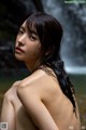 A naked woman standing in front of a waterfall.