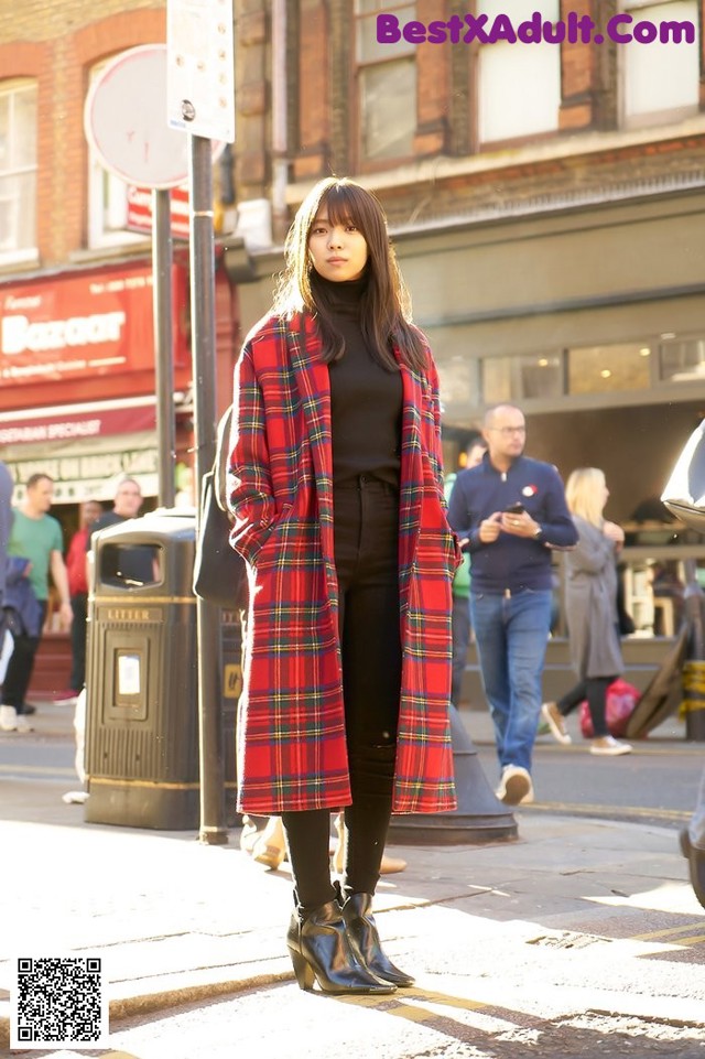 A woman in a red plaid coat is standing on the street.