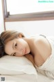 A woman laying on top of a bed next to a window.