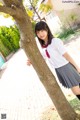 A woman in a school uniform leaning against a tree.