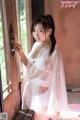 A woman in a white robe standing by a window.